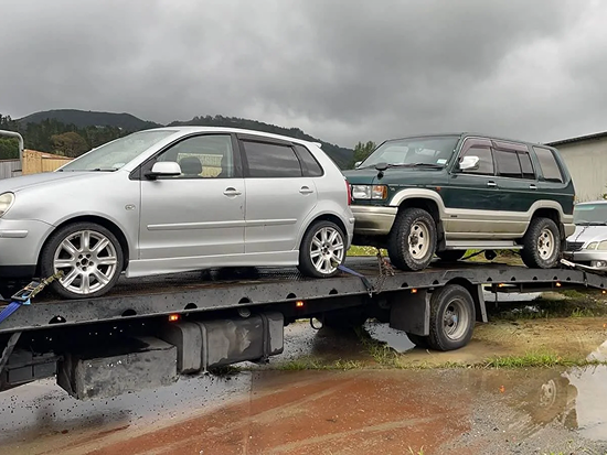Tow truck carrying two scrap cars for removal in Nelson